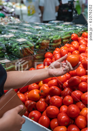 Woman holding purse and picking perfect tomato at grocery store 61076202