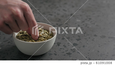 man hand takes pumpkin seeds from white bowl with copy space 61091008