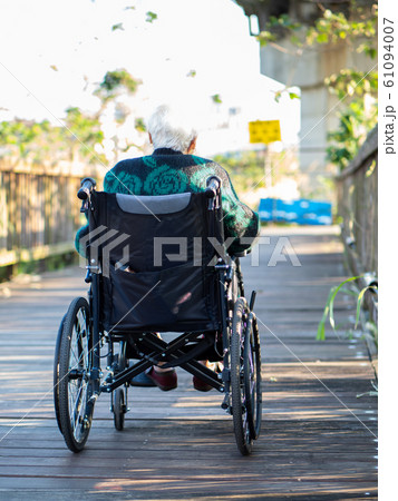 Elderly Asian women, elderly, sit on wheelchairs outdoors in the park. 61094007