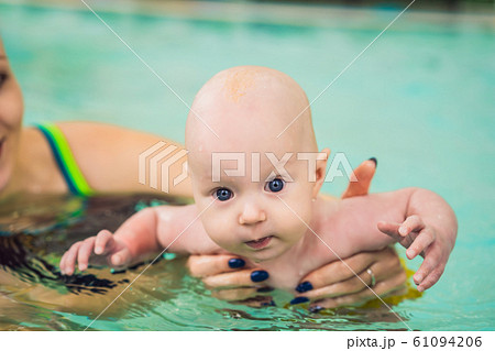 Beautiful mother teaching cute baby girl how to swim in a swimming pool. Child having fun in water 61094206
