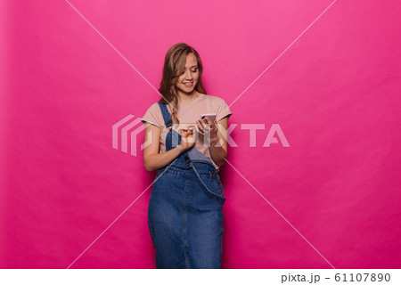 Cheerful young woman using mobile phone on isolated pink background. Cheerful young woman using mobile phone on isolated pink background. 61107890