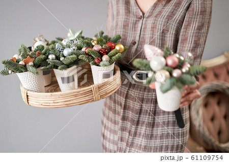 Florist holds a tray with christmas arrangements and one in his hand. Beautiful festive arrangement of fresh spruce in coffee Cup. Christmas mood. Florist holds a tray with christmas arrangements and one in his hand. Beautiful festive arrangement of fresh spruce in coffee Cup. Christmas mood. 61109754