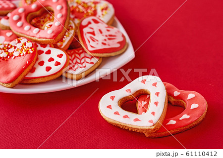 Decorated heart shape cookies in white plate and two cookies on red background Decorated heart shape cookies in white plate and two cookies on red background 61110412
