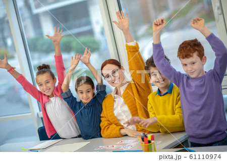 Teacher and children raising hands up at the class 61110974