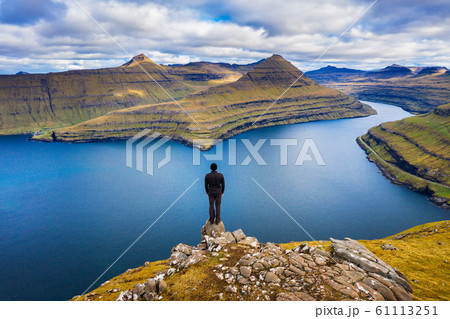 Hiker enjoys views over fjords from a mountain near Funningur on Faroe Islands 61113251