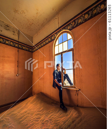 Tourist sits in the window of a room in the ghost town Kolmanskop, Namibia 61113265