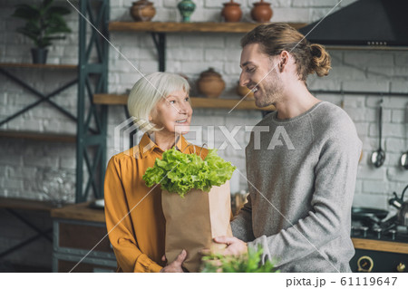 Young smiling man giving a package with greens to his mom 61119647