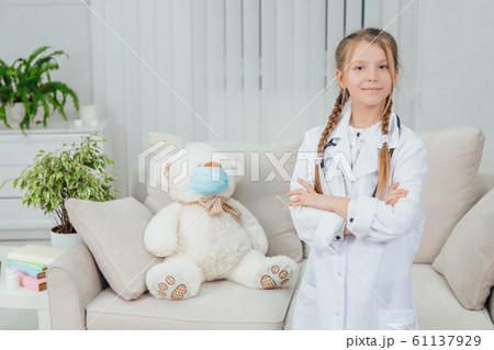 Pretty confident little girl wearing doctor coat, stethoscope standing, folding her hands, looking at the camera. 61137929