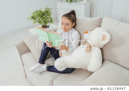 Cute little girl sitting on the sofa with teddy-bear near her, reading fairy-tale. Cute little girl sitting on the sofa with teddy-bear near her, reading fairy-tale. 61138447