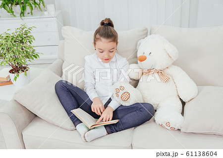 Cute little girl sitting on the sofa with teddy-bear near her, reading fairy-tale. Cute little girl sitting on the sofa with teddy-bear near her, reading fairy-tale. 61138604