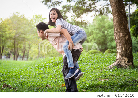 Happy asian father laugh giving piggyback ride to beautiful daughter having fun,hug together,smiling child girl enjoying active game with dad, young man carrying cute daughter on back,playing in outdo 61142010