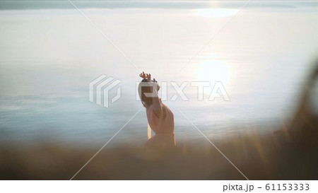 Freedom, youth, happiness. The girl rejoices in the rays of the sun on a background of water. Silhouette Model Posing On Water Texture. Dawn on the beach. Woman wearing a transparent orange dress 61153333