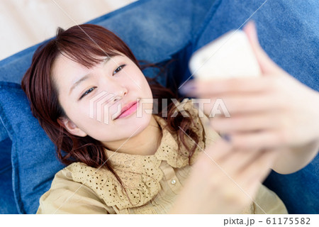 ソファで寝ながらスマホを操作する女性 61175582
