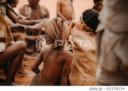 African kid from behind in social group of people sitting in traditional village 61178134