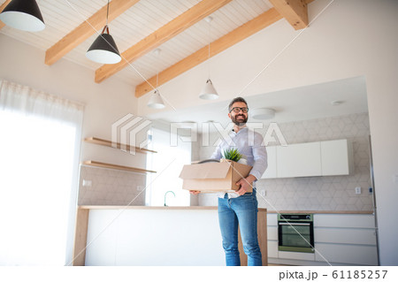 Mature man standing in unfurnished house, holding a moving box. Mature man standing in unfurnished house, holding a moving box. 61185257