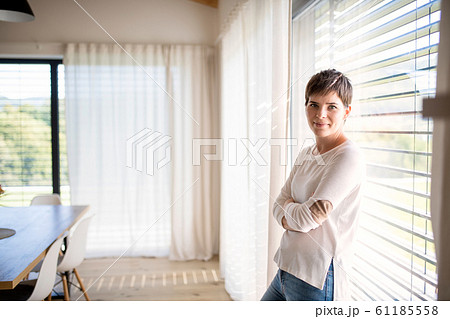 Portrait of young woman standing by window indoors at home, looking at camera. Portrait of young woman standing by window indoors at home, looking at camera. 61185558