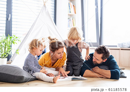 Young family with two small children indoors in bedroom reading a book. 61185578