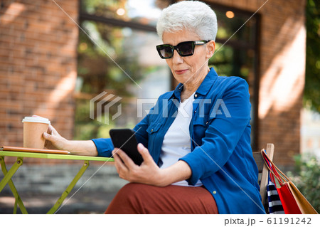 Smiling old woman using mobile phone on the street 61191242