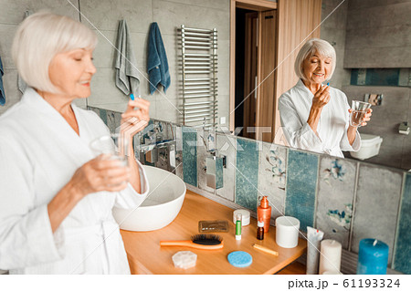 Cheerful old woman standing by the mirror and taking pills 61193324