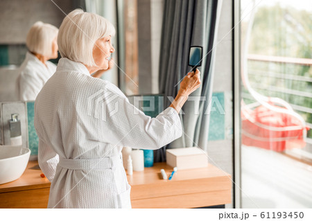 Smiling old lady in bathrobe looking in the mirror Smiling old lady in bathrobe looking in the mirror 61193450