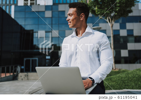Merry young man working on laptop outdoors stock photo 61195041