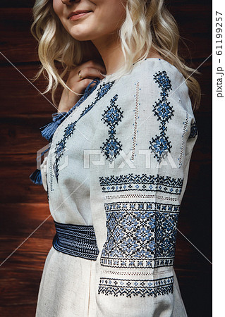 Beautiful bride in an embroidered shirt on the background of a wooden house. Pattern details 61199257