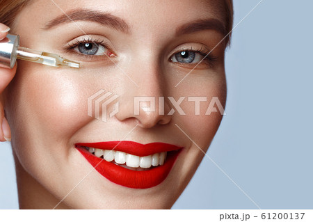 Beautiful girl with red lips and classic makeup with oil for skin in hand. Beauty face. Beautiful girl with red lips and classic makeup with oil for skin in hand. Beauty face. 61200137