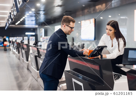 Business trip. Handsome young businessman in suit holding his passport and talking to woman at airline check in counter in the airport 61201165