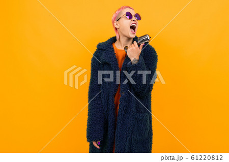 Extraordinary beautiful woman with short pink hair in dark coat and sunglasses sings into a 61220812