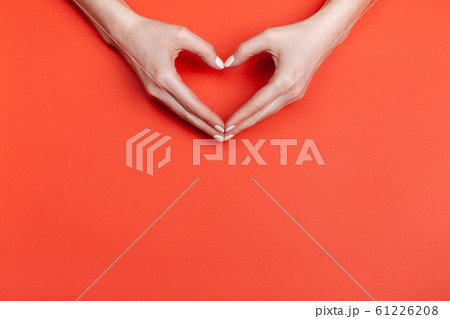Female hands show a heart symbol on a red background. Place for text 61226208