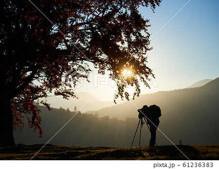 Hiker tourist man with camera on grassy valley on background of mountain landscape under big tree. 61236383