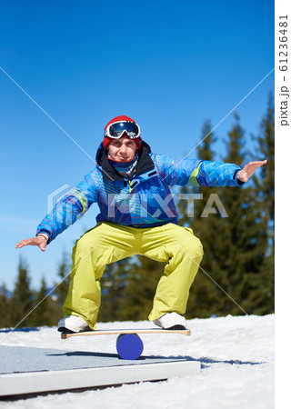 Male snowboarder balancing on snowboard in white snow on background of blue sky and spruce trees. Male snowboarder balancing on snowboard in white snow on background of blue sky and spruce trees. 61236481