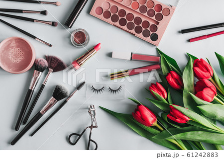 Makeup cosmetics and red peony flowers on a blue background. Brushes, shadow palette, lipstick and eyelashes for the care and beauty of a woman's face 61242883