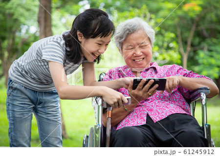 Happy asian senior grandmother and little child girl using cellphone together,playing video game on smart phone,smiling elderly woman in wheelchair,granddaughter having fun,talk in outdoor park,family 61245912