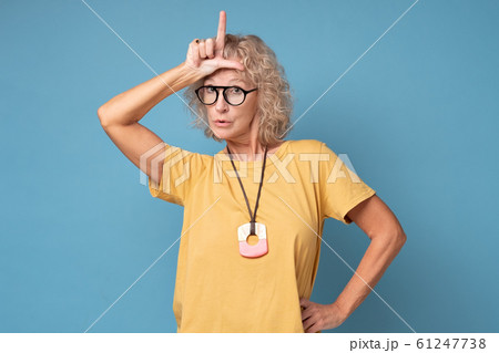 Annoyed woman, showing loser sign standing with disrespectful expression 61247738