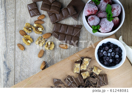 Pieces of chocolate together with chocolates on the wooden table together with strawberries, blueberries and walnuts Pieces of chocolate together with chocolates on the wooden table together with strawberries, blueberries and walnuts 61248081