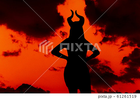 Horned devil woman on a background of black clouds and sky fiery red. Horned devil woman on a background of black clouds and sky fiery red. 61261519