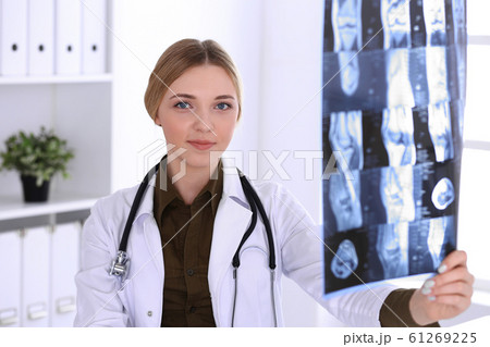 Doctor woman examining x-ray picture near window in hospital. Surgeon or orthopedist at work. Medicine and healthcare concept. Khaki colored blouse of a therapist looks good 61269225