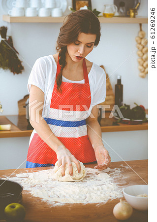 Young brunette woman cooking pizza or handmade pasta in the kitchen. Housewife preparing dough on wooden table. Dieting, food and health concept Young brunette woman cooking pizza or handmade pasta in the kitchen. Housewife preparing dough on wooden table. Dieting, food and health concept 61269246