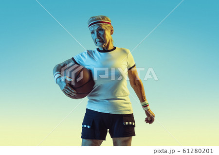 Senior woman playing basketball in sportwear on gradient background in neon light 61280201