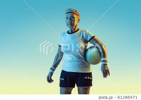 Senior woman training in volleyball in sportwear on gradient background in neon light 61280471