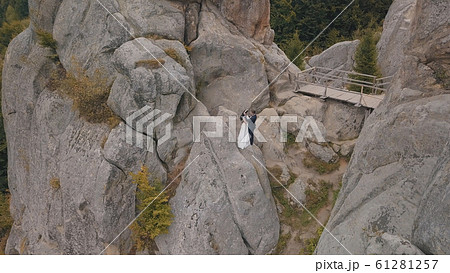 Newlyweds stand on a high slope of the mountain. Groom and bride. Aerial view 61281257