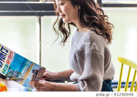 窓辺で旅行の計画をする女性  （旅行パンフレットは撮影のために作成されたダミーです。） 61290046