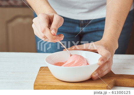 Woman whisking red cream for decorating cookies 61300125