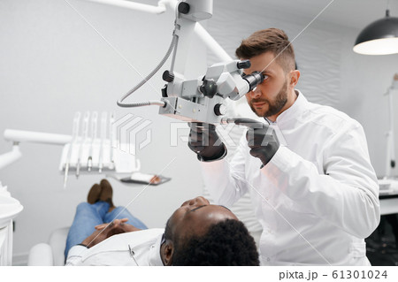 Male dentist examining teeth of male patient in clinic 61301024