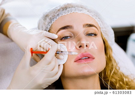 Female doctor cosmetologist in white rubber gloves makes lip augmentation procedure of a beautiful woman in modern beauty salon. Cosmetology skin care. Close-up portrait 61303083