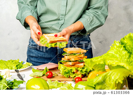 Woman is cooking tasty sandwich with ham and vegetables in the kitchen. 61303366