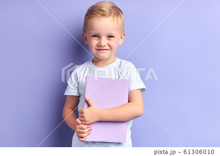 Little shy boy holding book isolated on purple background 61306010