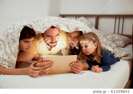 friendly caucasian family under blanket on bed watching videos friendly caucasian family under blanket on bed watching videos 61309842