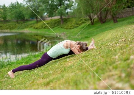 A young sports girl practices yoga on a green lawn A young sports girl practices yoga on a green lawn 61310398